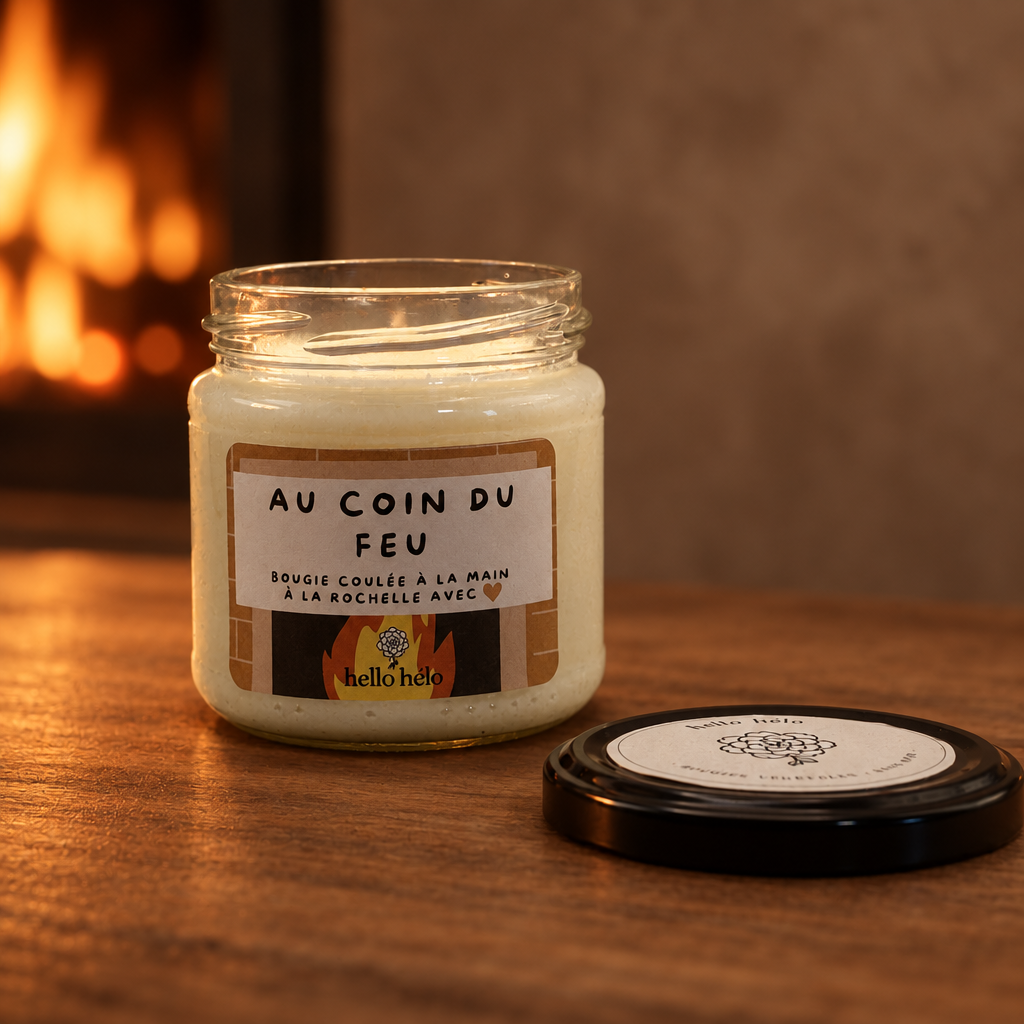 Bougie artisanale Au coin du feu, pot en verre ouvert avec son couvercle noir posé à côté, sur une table en bois près d'une cheminée
