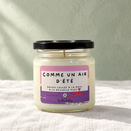 Bougie artisanale Comme un air d'été, pot en verre fermé avec étiquette violette et rose, sur un lin blanc devant un mur vert sauge